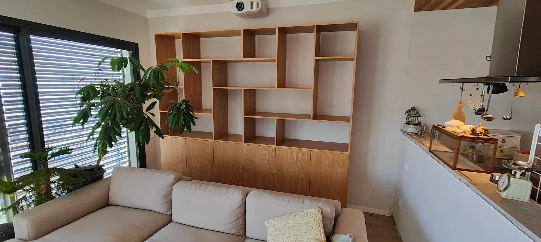 יחידת מדפים אסימטרית מפורניר אלון עם ארוניות סגורות בתחתית, לאורך קיר בסלון מעל ספה בז'